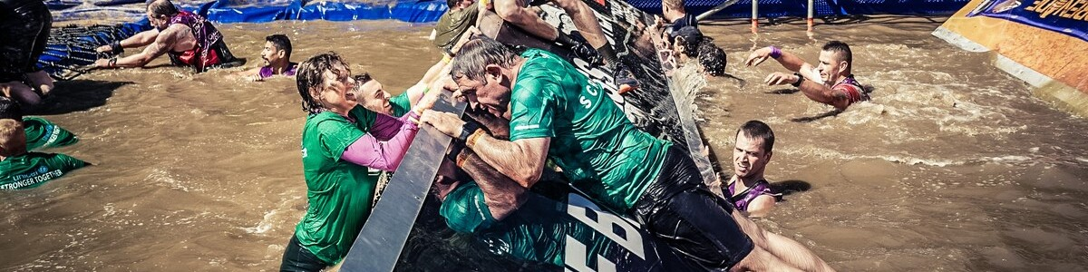Macmillan participants at a Tough Mudder helping each over a water obstacle
