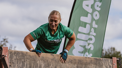 A woman wearing a Macmillan t-shirt over a wall obstacle.
