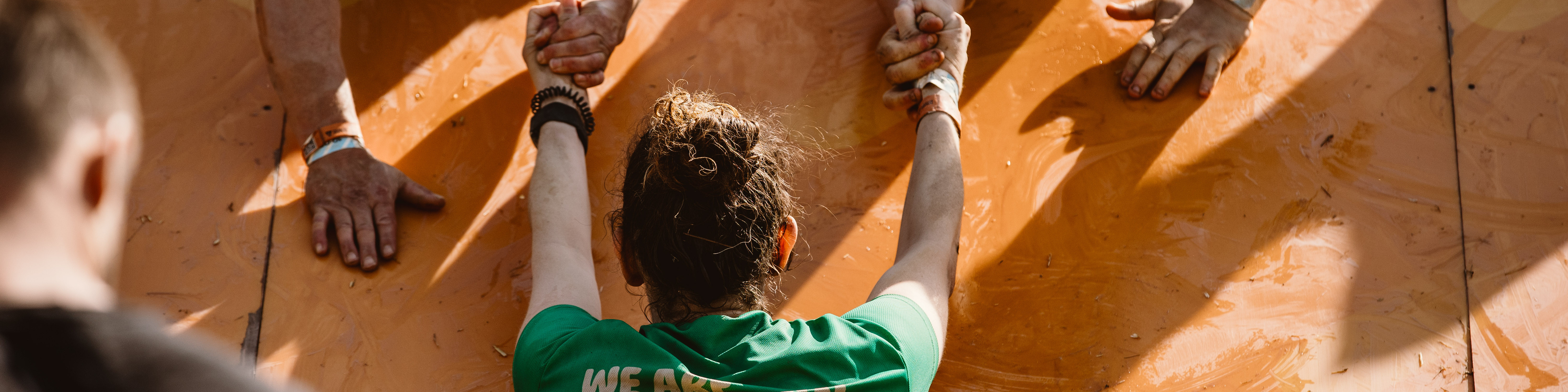 Someone wearing a Macmillan t-shirt being helped by two other people up a wall.