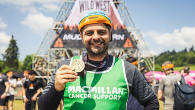 A man wearing a Macmillan t-shirt posing with his Tough Mudder medal