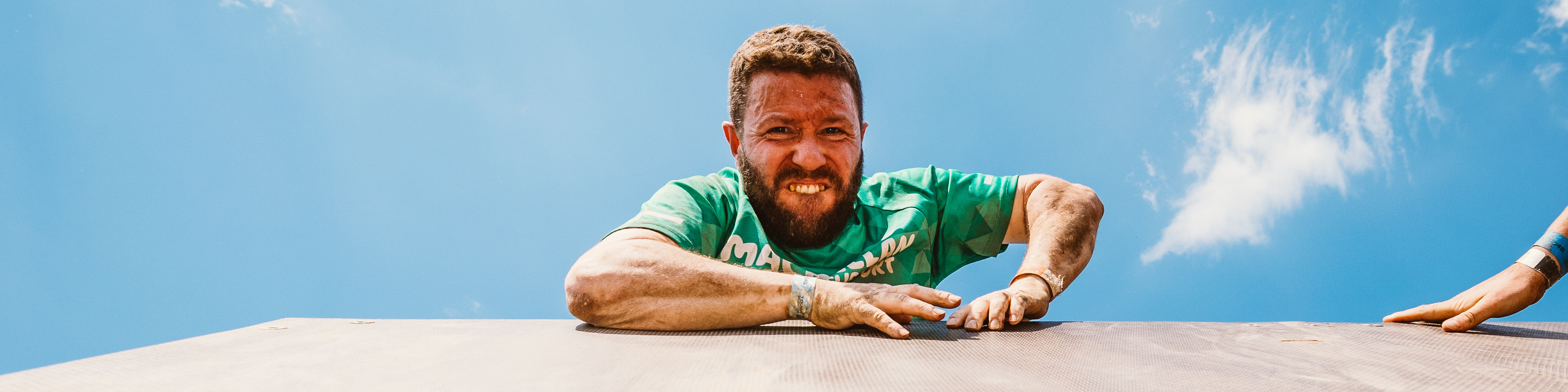 A man wearing a Macmillan t-shirt looking down as he climbs over a wall obstacle