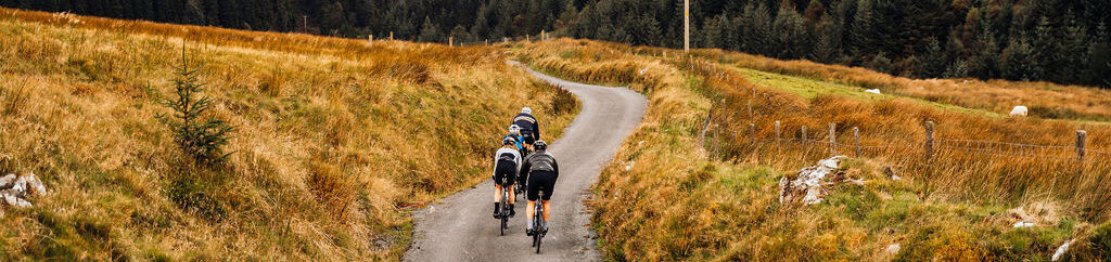 View from behind of 3 cyclists gliding down a path surrounded by fields and hills.
