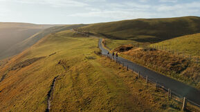 Distance shot of quiet road on a hillside. 3 cyclists can just been seen.