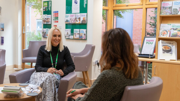 2 people talking in a therapeutic setting. There are leaflets about cancer on the shelves around them.