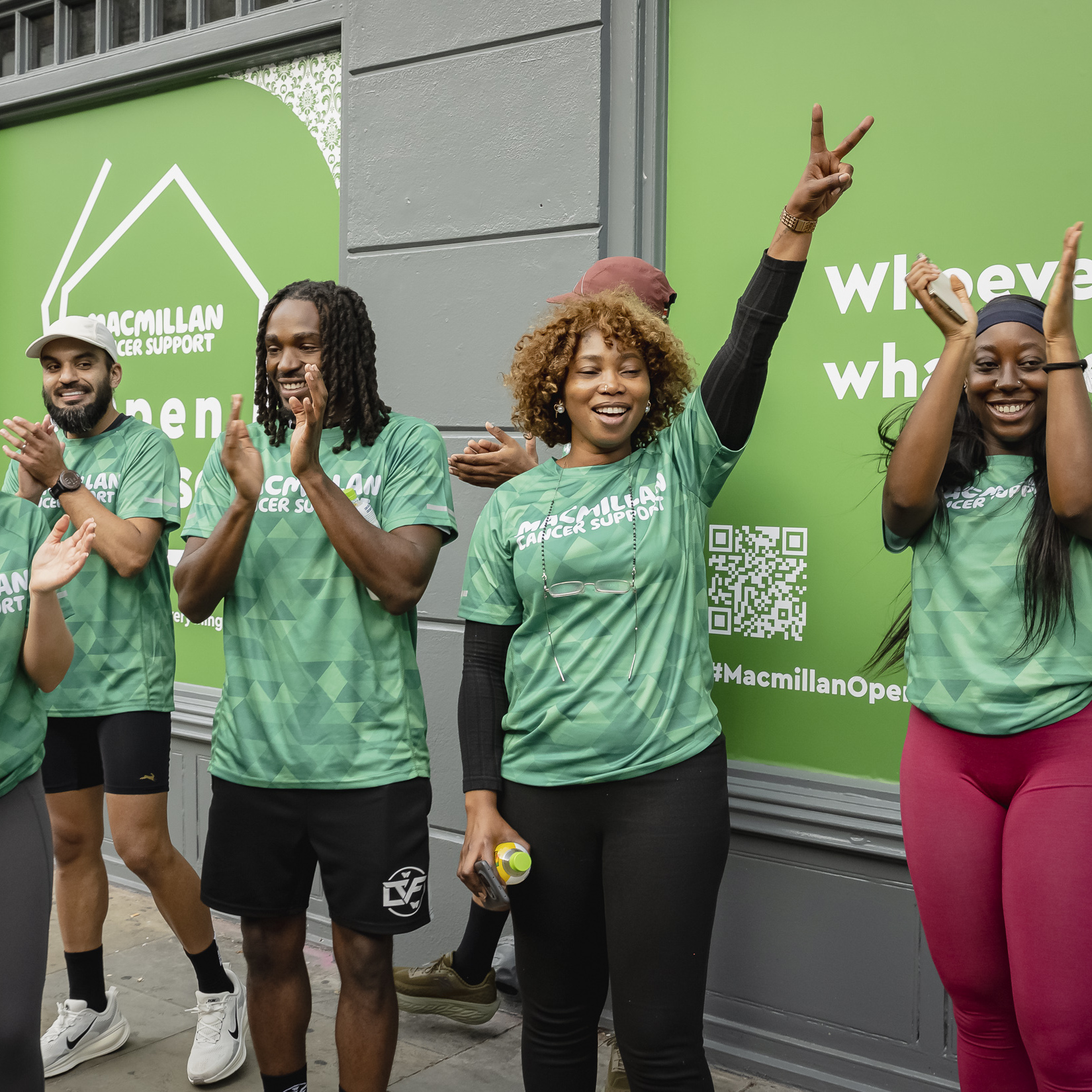 Group of participants in green Macmillan Cancer Support shirts clapping and cheering outside the venue.