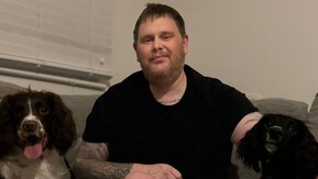 A white man with light brown hair and a beard sitting with his 2 dogs.