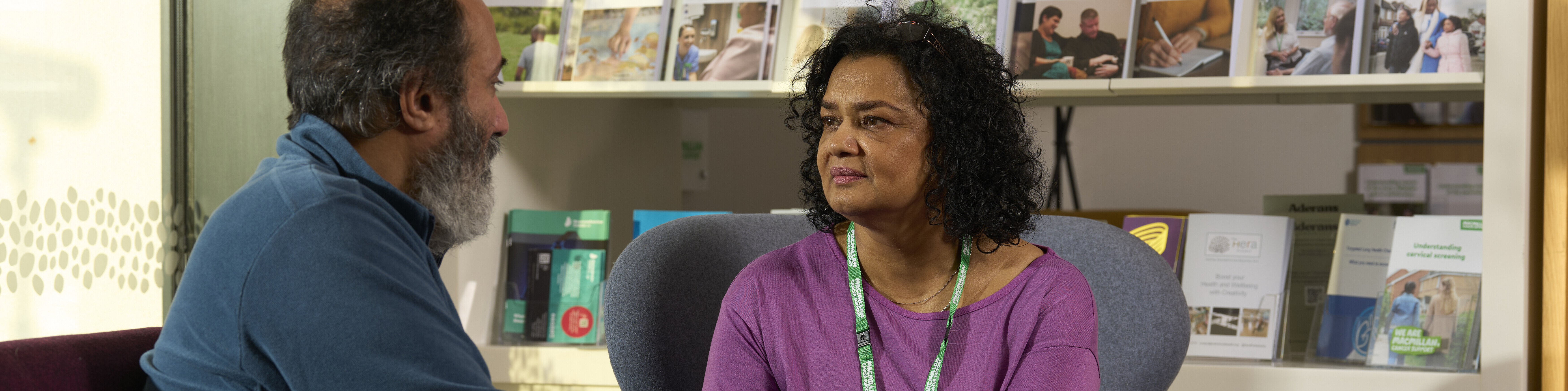 A Macmillan support worker with a patient at an information and support centre. They are holding their hand in a comforting way.