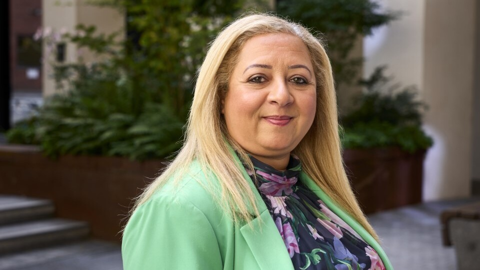 Rasha is standing outside. She has long hair and is wearing a floral top and green blazer. 