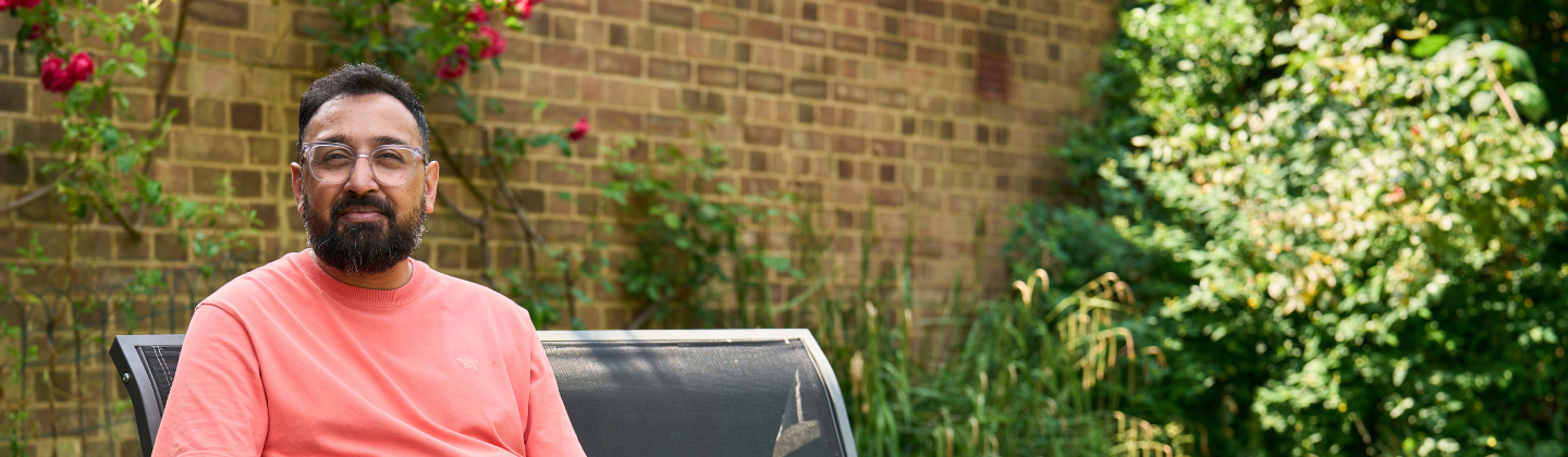 Mohammed has short dark hair and a beard, he is sat outside in his garden.