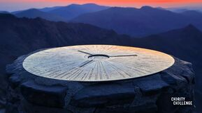 Toposcope on top of Mount Snowdon. Behind it is a view of the mountains and the sun setting.