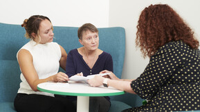 Three women sat around a round table engaged in a conversation. 
