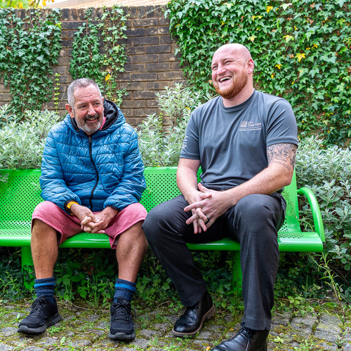 A link worker and a client from CRT Together are sitting on a bench outside laughing together  