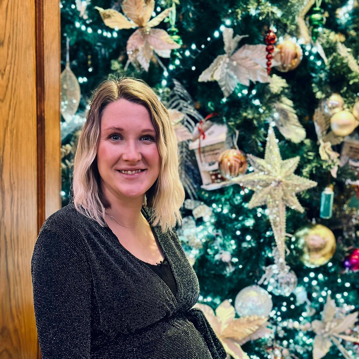 Woman with blonde hair standing in front of Christmas tree