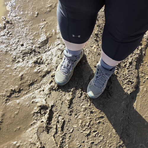 A person wearing hiking boots standing on a muddy path.