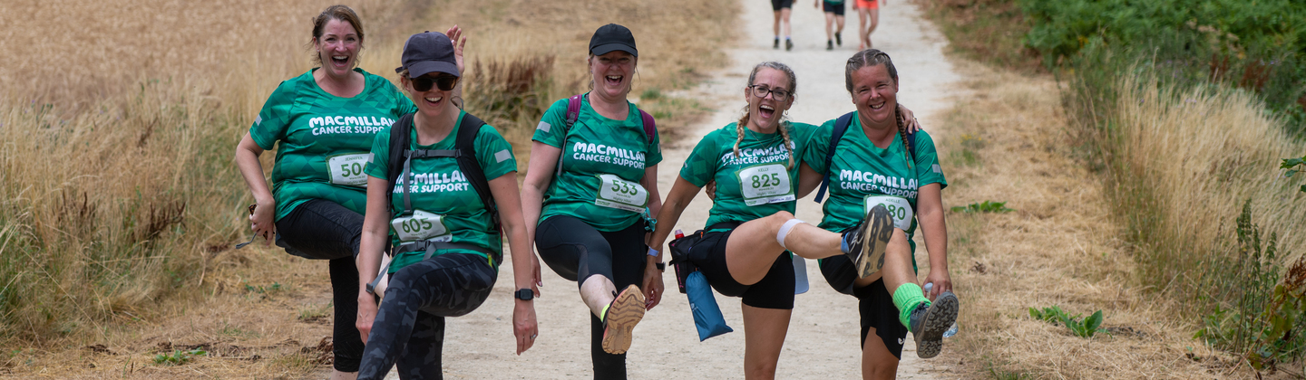 A team of five Mighty Hikers smiling at the camera and doing leg kicks