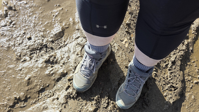 A person wearing hiking boots standing on a muddy path.