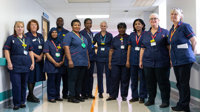 Group of nurses wearing dark blue uniforms stand in line in a hospital setting.