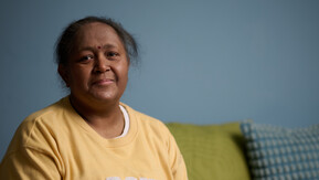 Indian lady sat on a sofa with a yellow jumper.