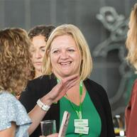 A smiling woman with shoulder length blonde hair talks to people in a conference setting