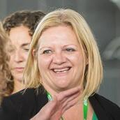 A smiling woman with shoulder length blonde hair talks to people in a conference setting