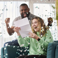 A man and a woman cheering having read a letter saying they've won the raffle. Confetti flies around them.