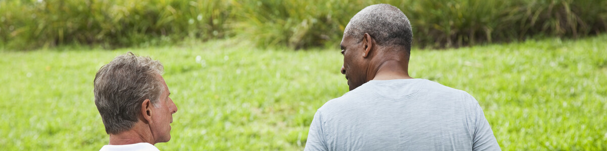Two men in conversation walking outdoors. They both have their back towards the camera.