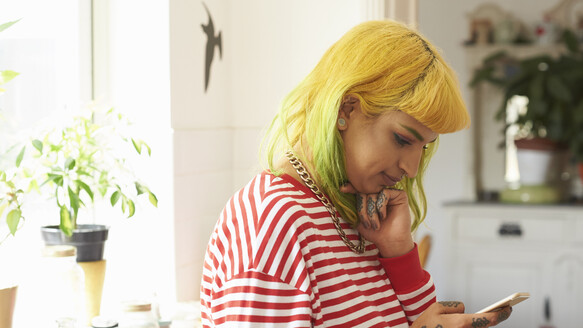 A person with brightly died hair and tattoos on their hands is looking at their mobile phone