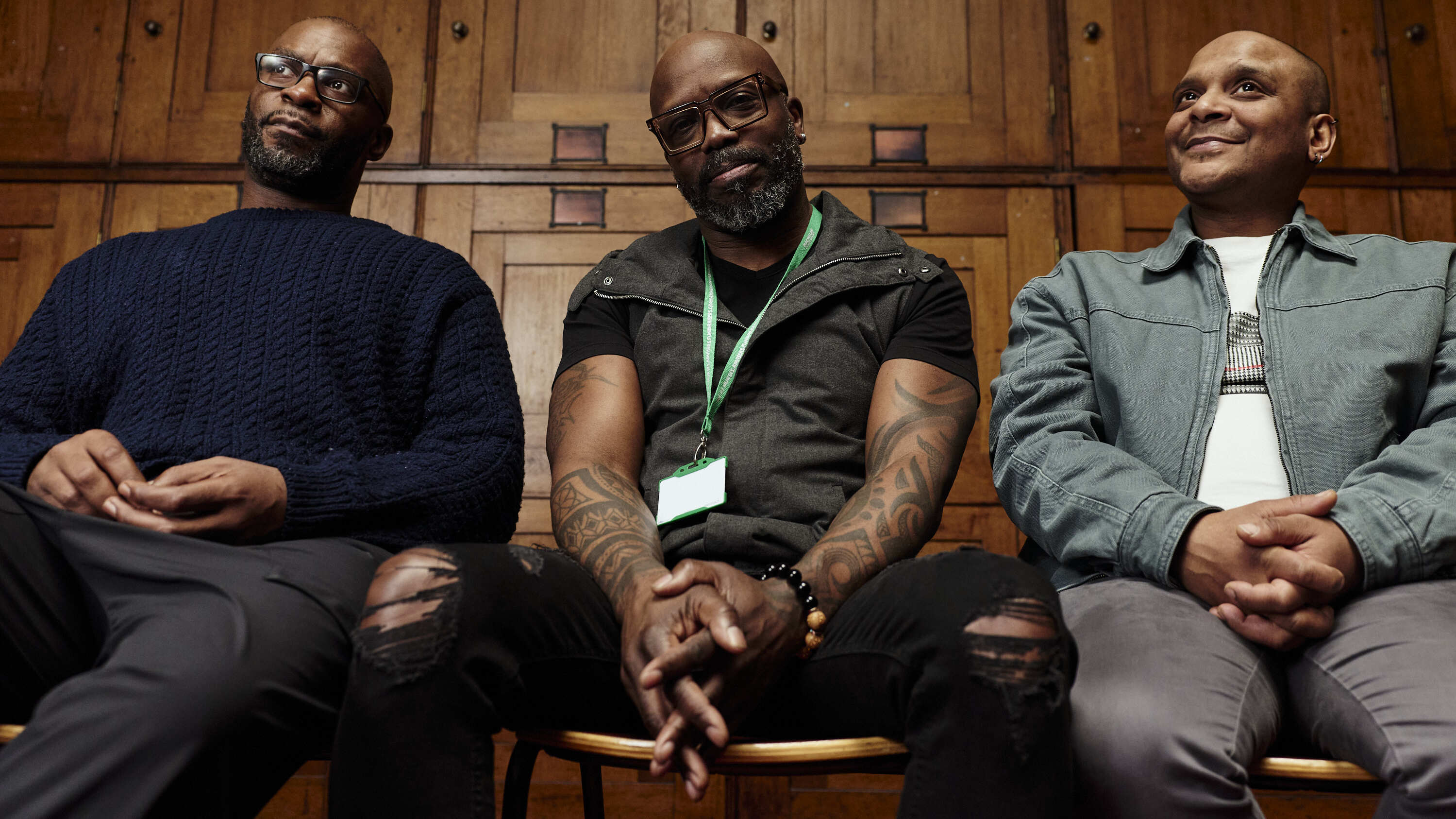 Three people sit side by side in a wood‑panelled room. The person in the middle is wearing a green Macmillan lanyard.