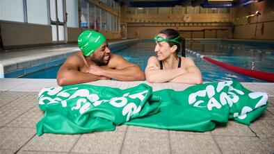 A man and a woman in a swimming pool at one end talking and smiling to each other. A Macmillan towel is on the edge of the pool in front of them