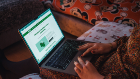 A close-up of hands using a laptop on a sofa, with a webpage open on the screen.