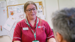 A healthcare professional hands a leaflet to someone seated in a clinical setting.