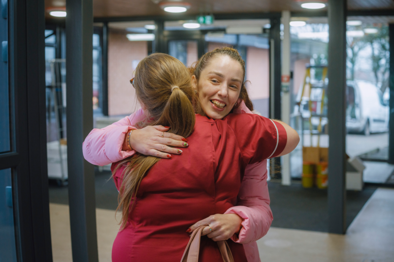 Two people embrace in a building entrance or corridor.