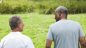 Two men in conversation walking outdoors. They both have their back towards the camera.