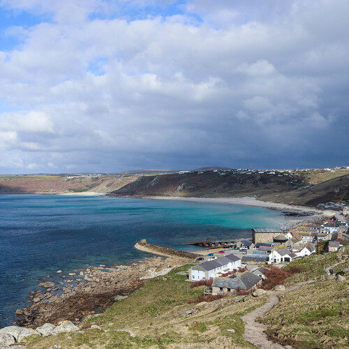 A rocky path goes downhill towards houses along a coast in Cornwall. 