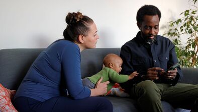 A couple and their baby are sitting on a sofa looking at a message on a mobile phone.