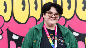 A person standing in front of a colourful wall filled with graffiti 