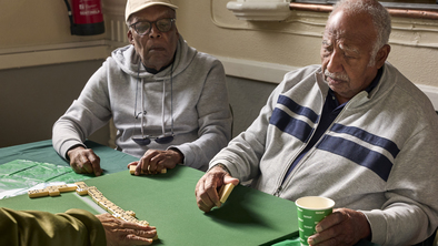 A group of men are playing dominoes at a Coffee Morning. They are sat at a table and concentrating on the game.