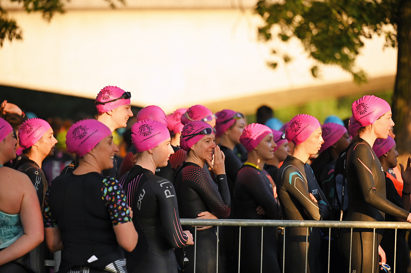 Group of women wearing pink swimming hats and wetsuits standing in a crowd