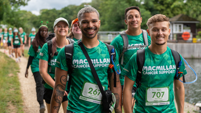 A group of people are hiking together down a path. They are all wearing bright green Macmillan branded tops.