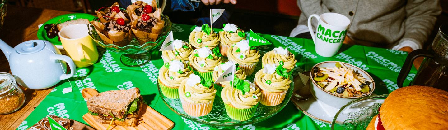 A clear cake stand is topped with delectable vanilla and matcha cupcakes. The cupcakes are topped with rich frosting and decorations.
