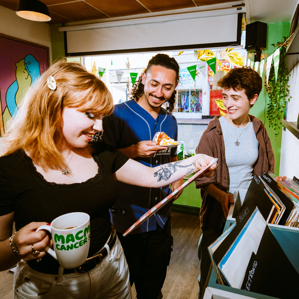 Three people are standing together in a vinyl shop. One person is looking at a vinyl from a stack. The shop has been decorated for a Coffee Morning.