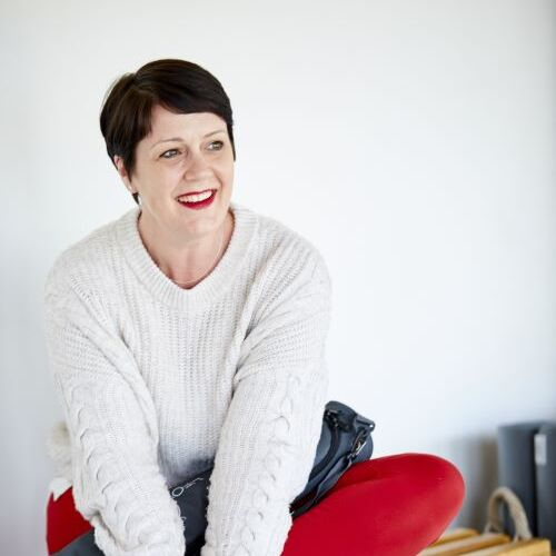 Woman sitting on bench wearing cream jumper smiling away from camera.