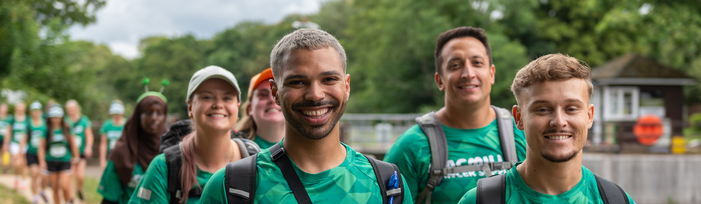 A group of people are hiking together down a path. They are all wearing bright green Macmillan branded tops.