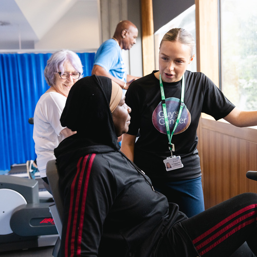 Physiotherapist Isla is standing next to an exercise bike. A patient is using the machine. Behind Isla are other patients using different exercise machines.