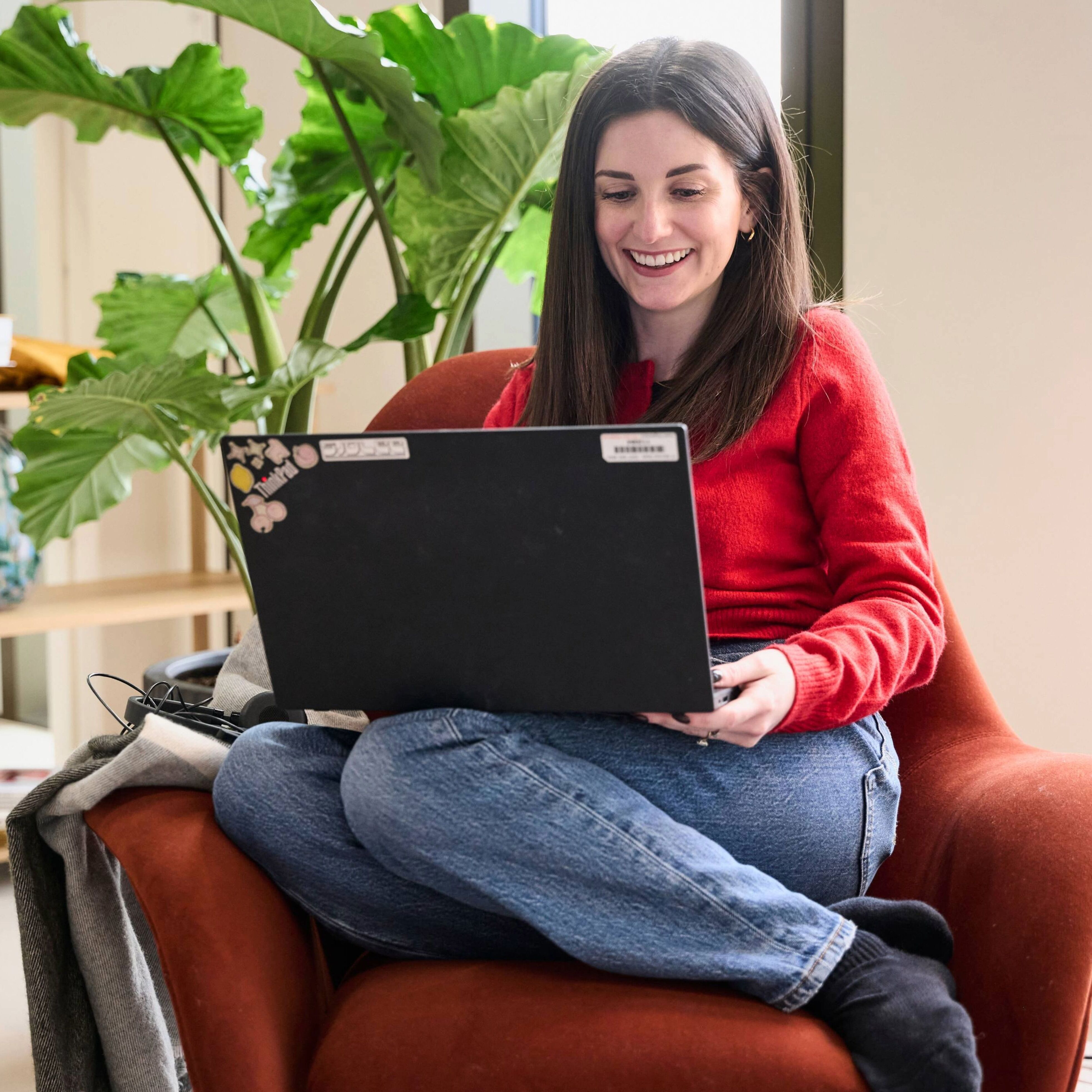 Employee sitting in a comfortable chair using a laptop in a bright office space with plants.