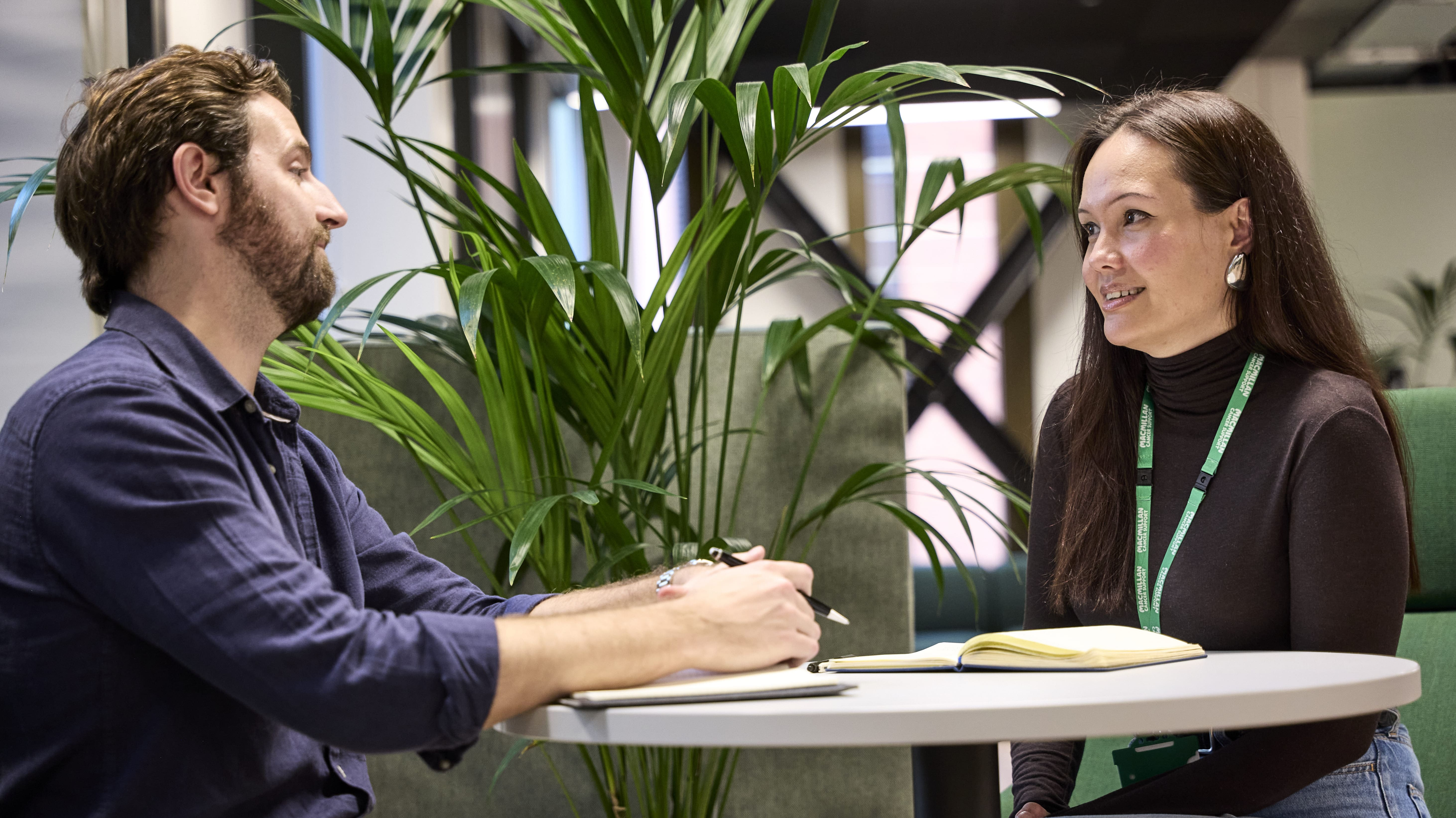 Two colleagues having a one-to-one discussion at a table in an office.