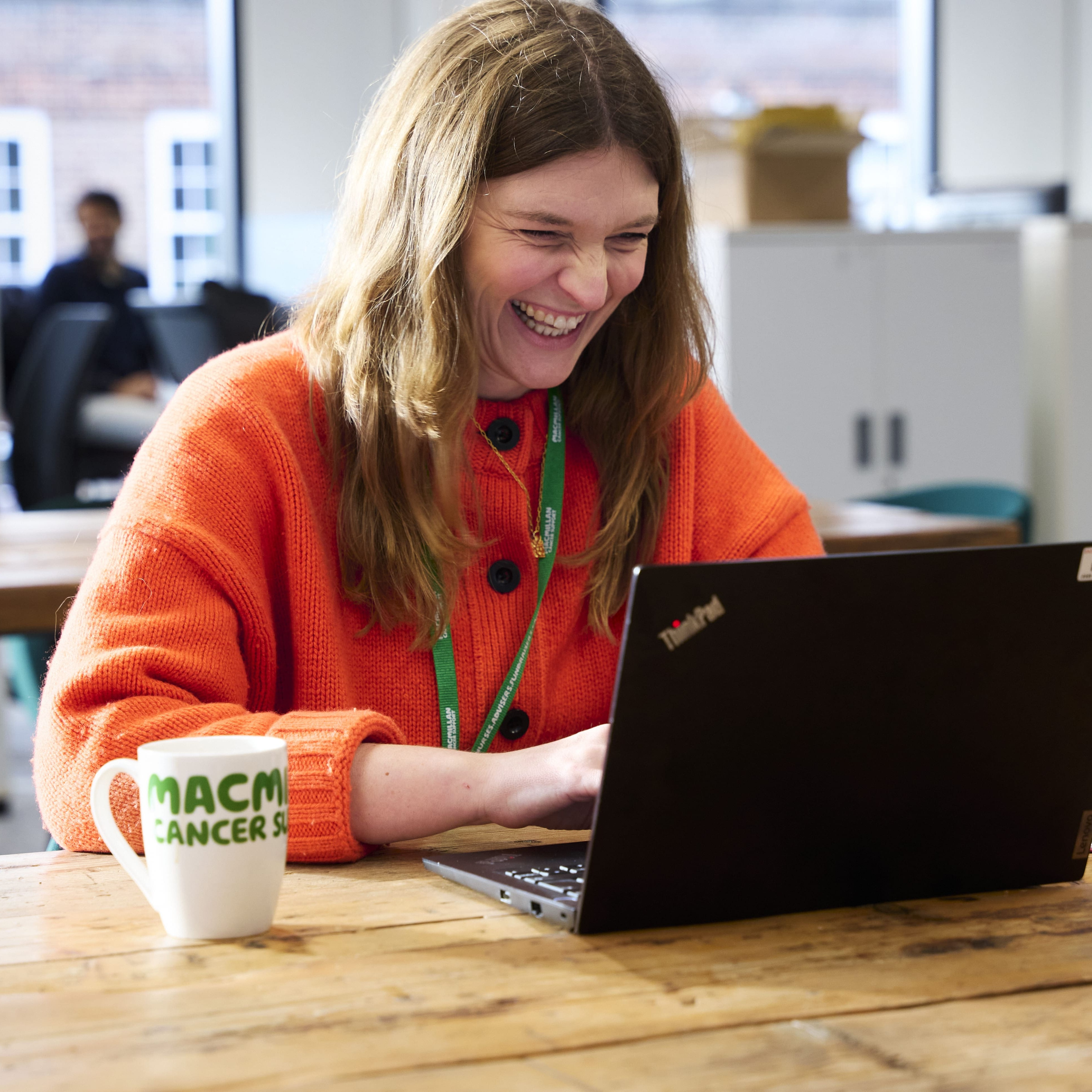 Employee working on a laptop at a shared table in an office.