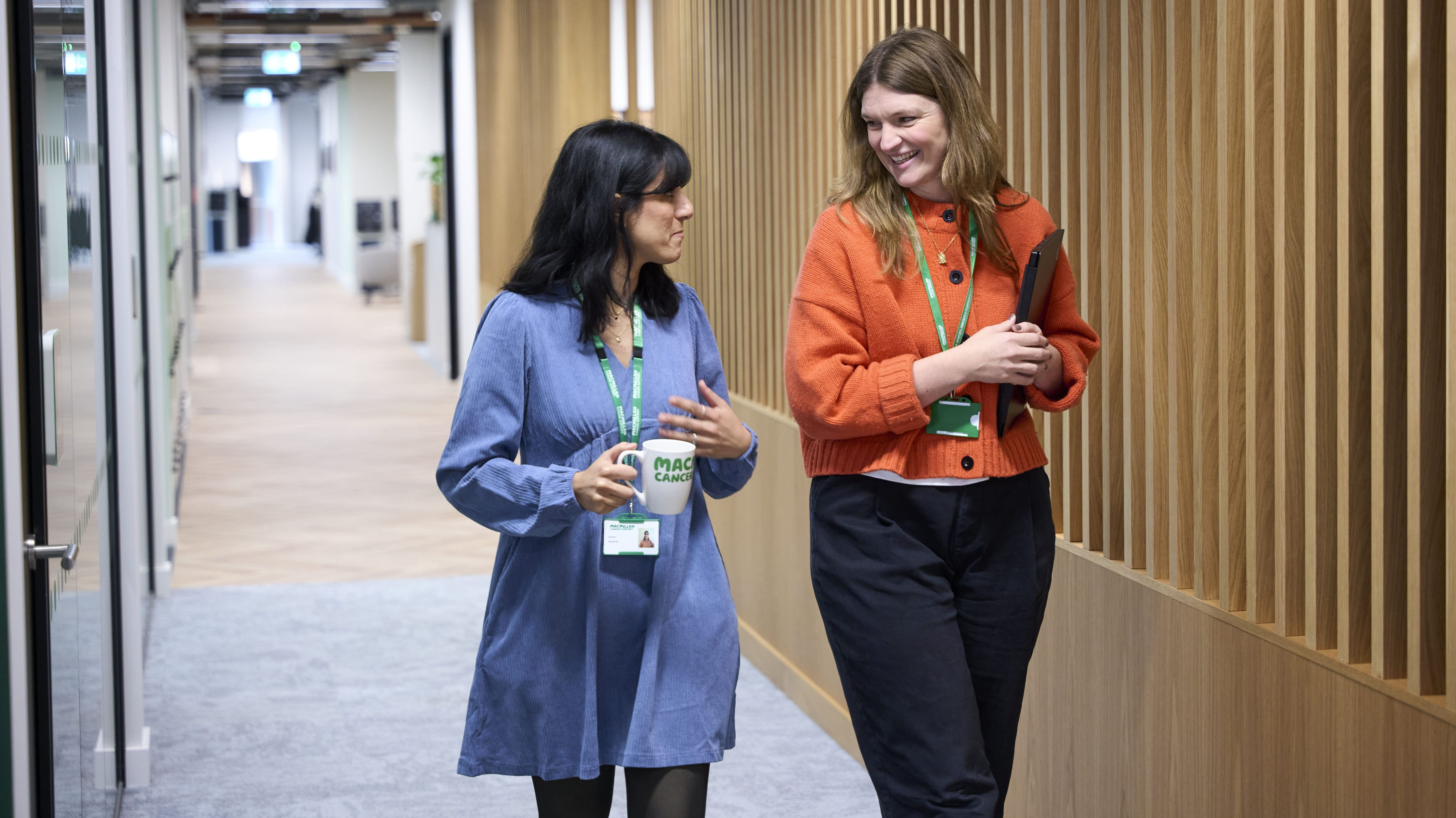 Two colleagues walking through an office corridor while talking.