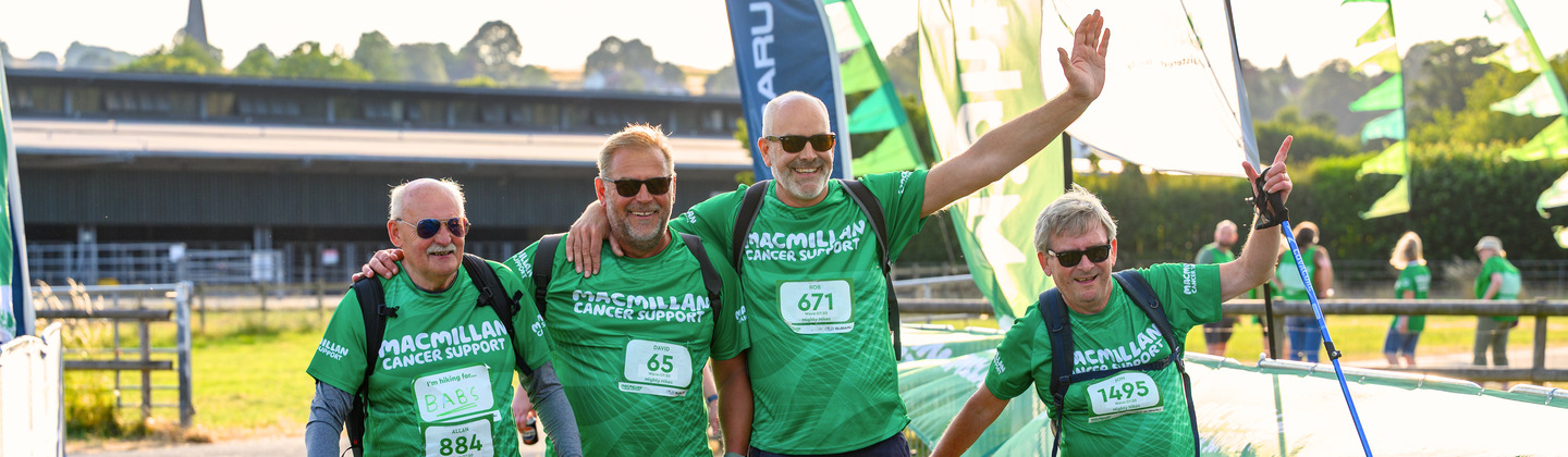 A group of Mighty Hikers crossing over the finish line at the Peak District Mighty Hike. They are all wearing green Macmillan branded tops and other hiking gear.