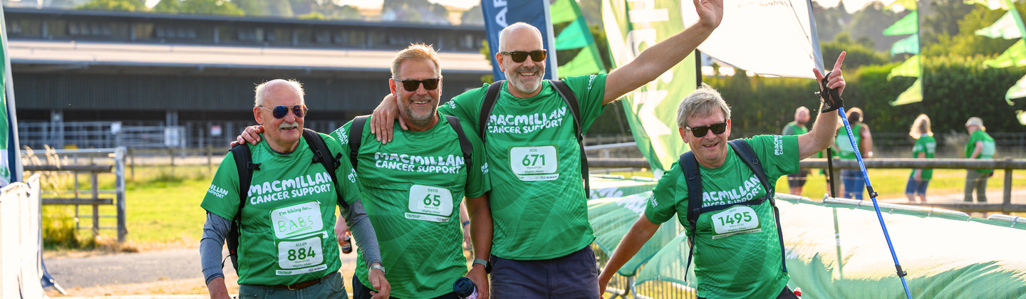 A group of Mighty Hikers crossing over the finish line at the Peak District Mighty Hike. They are all wearing green Macmillan branded tops and other hiking gear.